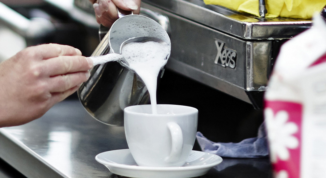 Barista expertly pouring steamed milk into a white cup in a coffee shop setting