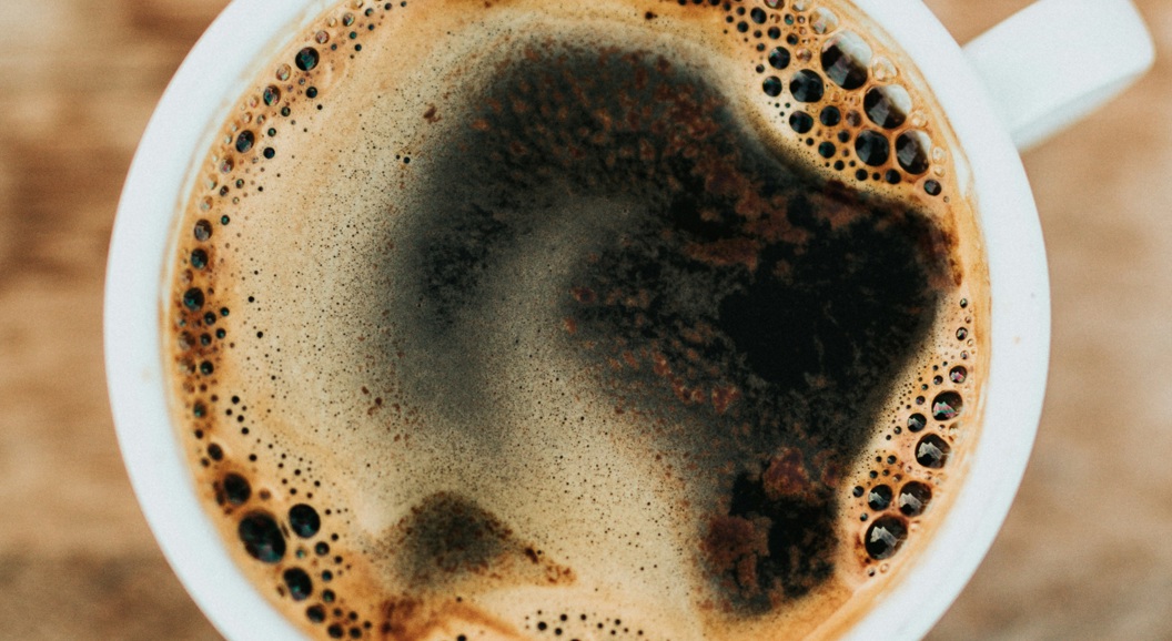 Toppvisning av en rykende svart kaffe i en hvit krus på et rustikt trebord