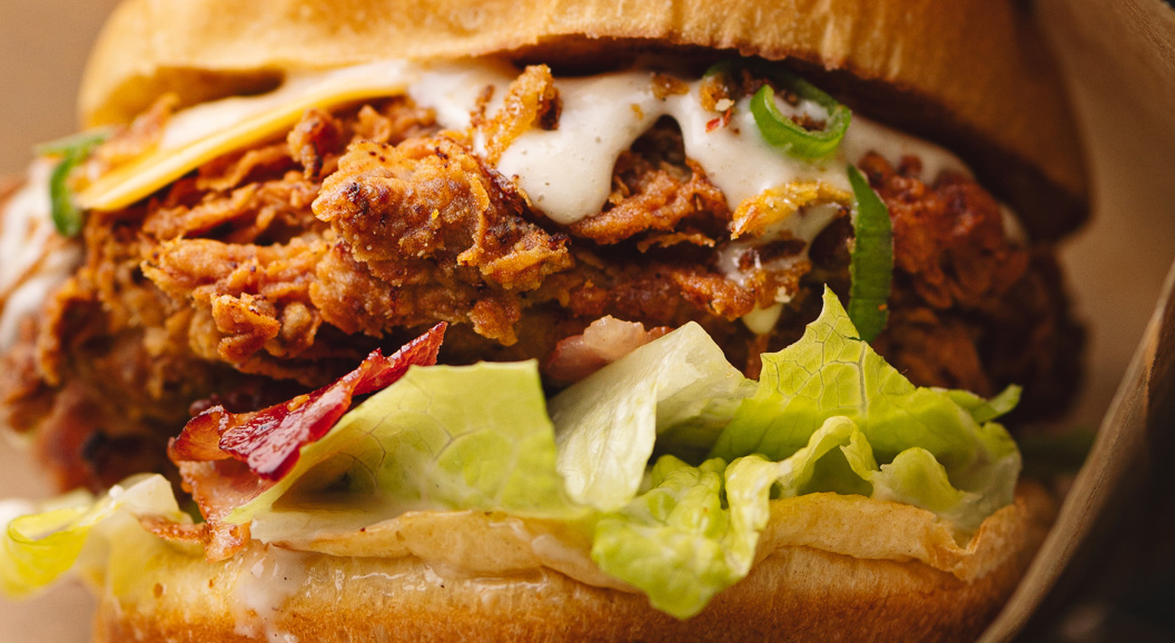 Close-up of a crispy fried chicken sandwich with lettuce, bacon, and creamy sauce on a toasted bun