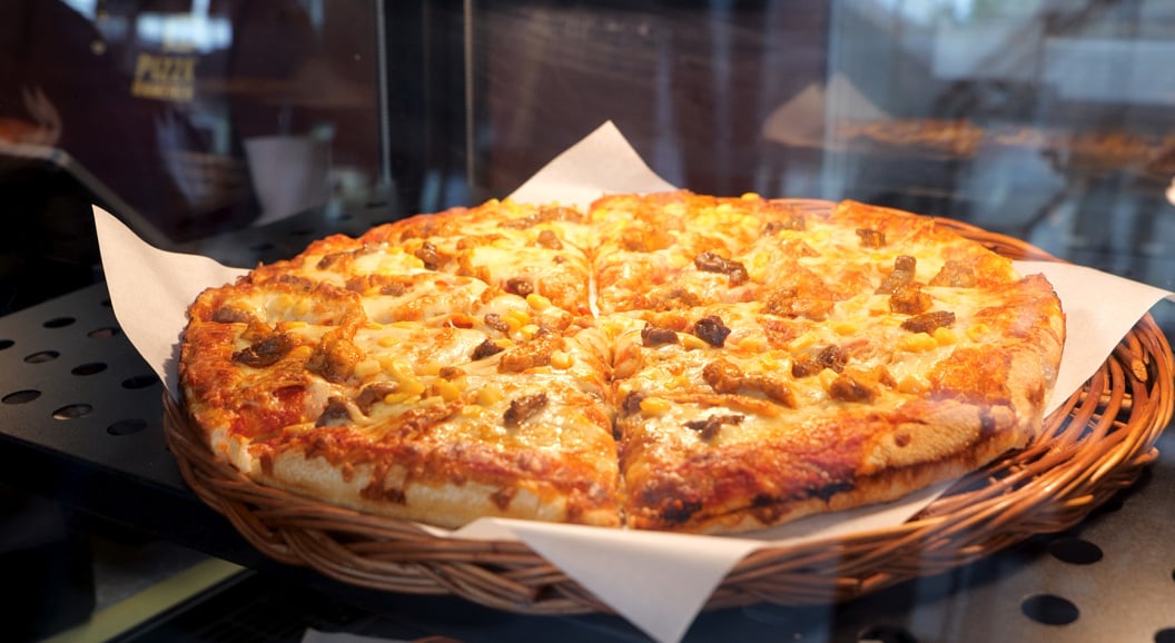 Freshly baked pizza with a cheesy topping and mushrooms, displayed in a wicker basket on parchment paper