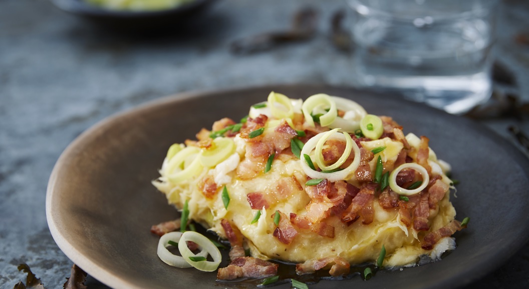Creamy potato casserole topped with crispy bacon and fresh green onions, served on a rustic ceramic plate