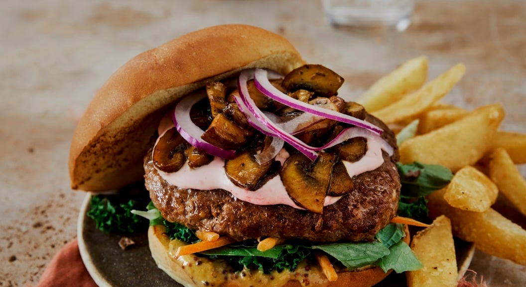 Saftig burger med sopp, rødløk og grønt på en tallerken, servert med grove pommes frites
