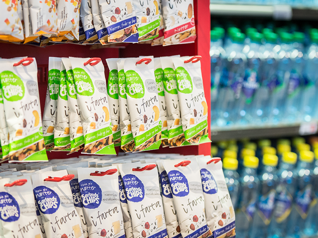 Snack bags displayed on a red shelf in a grocery store aisle with bottles of water in the background