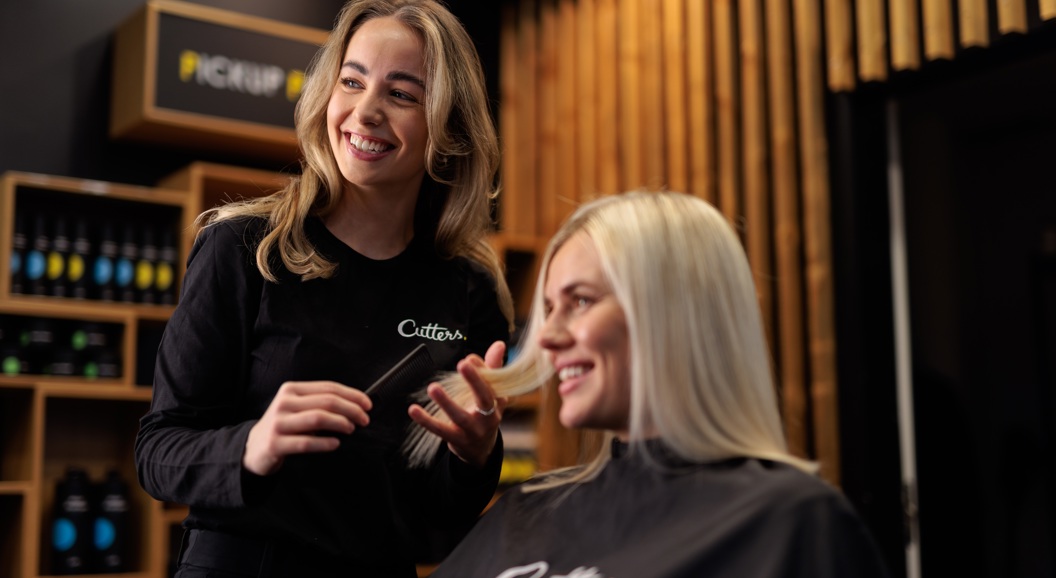 Smiling hairstylist with long hair serving a blonde client in a modern salon