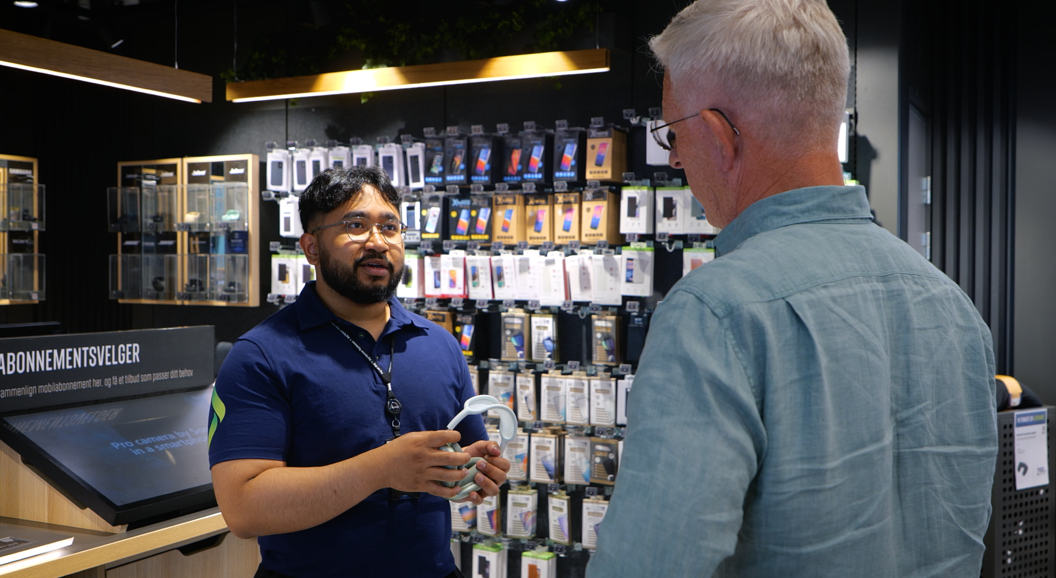 Store employee assisting a customer with earphones in a modern electronics shop, surrounded by phone accessories