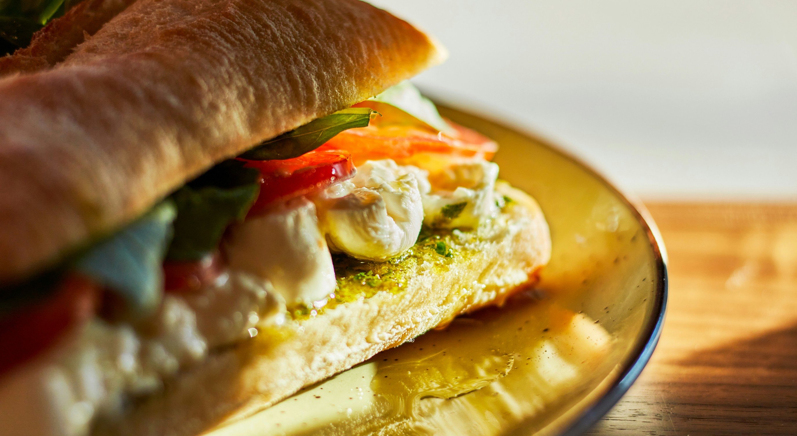 Fersk sandwich med mozzarella, tomater, basilikum og pesto på en tallerken i varm sollys