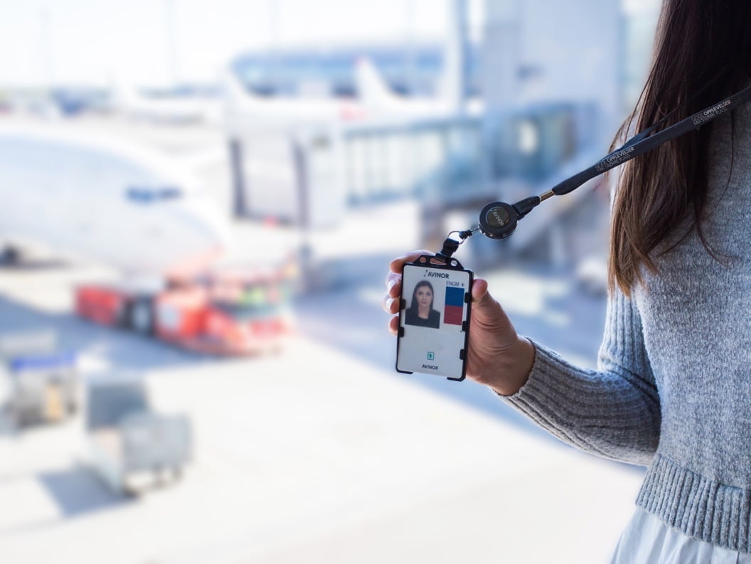 Kvinne som holder ansatt-ID i flyplassterminal med fly i bakgrunnen