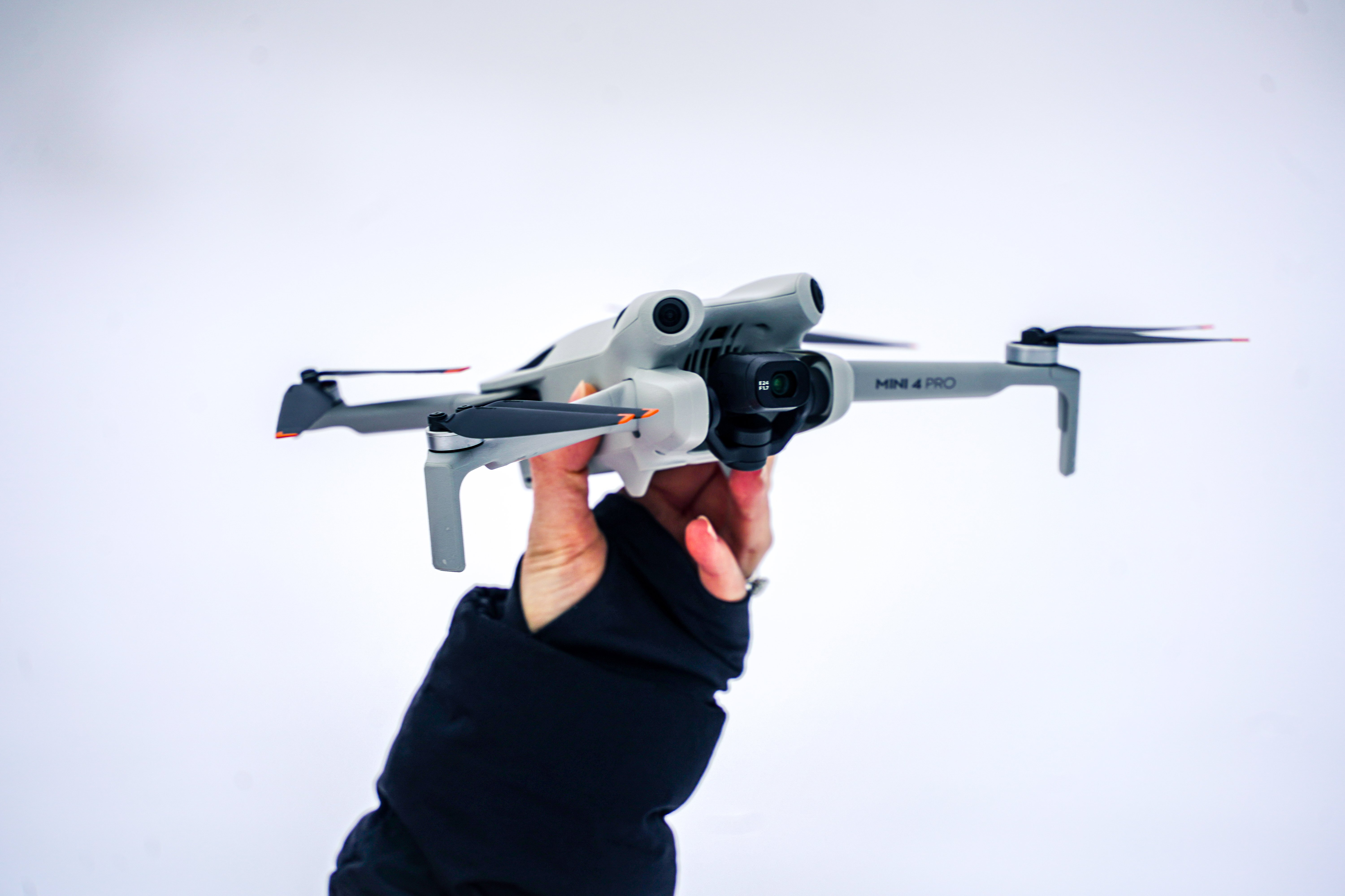 Hånd holder en grå drone av typen Mini 4 Pro mot en hvit bakgrunn, klar for takeoff.