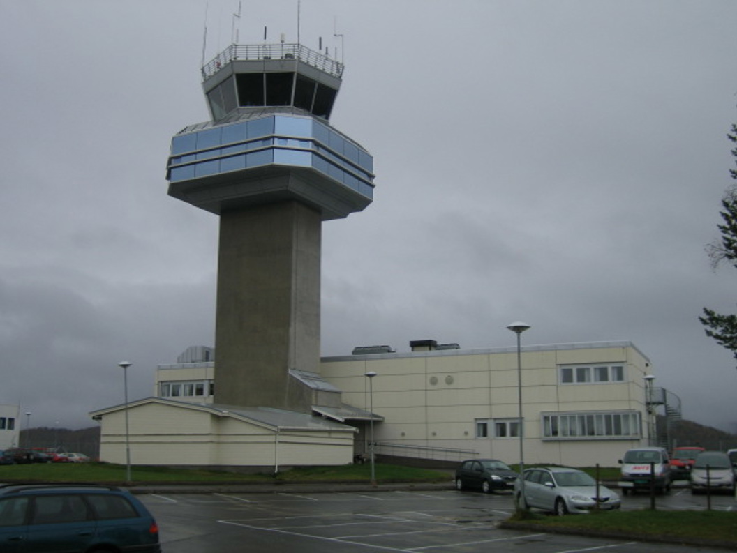 Kontrolltårn ved Bardufoss flyplass omgitt av overskyet himmel og parkerte biler.