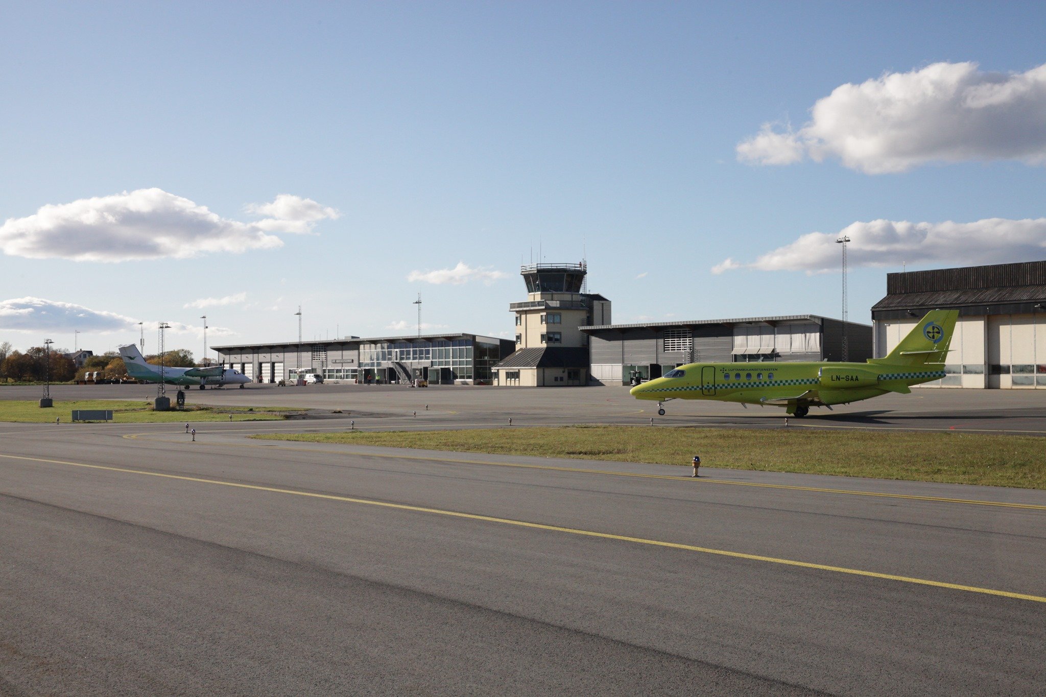 To fly på flyplassen i klart vær med flytårn og hangarer i bakgrunnen.