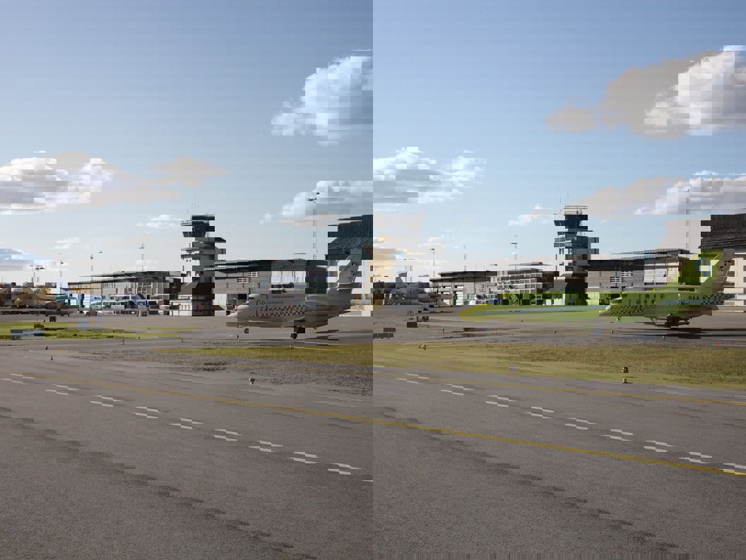 To fly på flyplassen i klart vær med flytårn og hangarer i bakgrunnen.