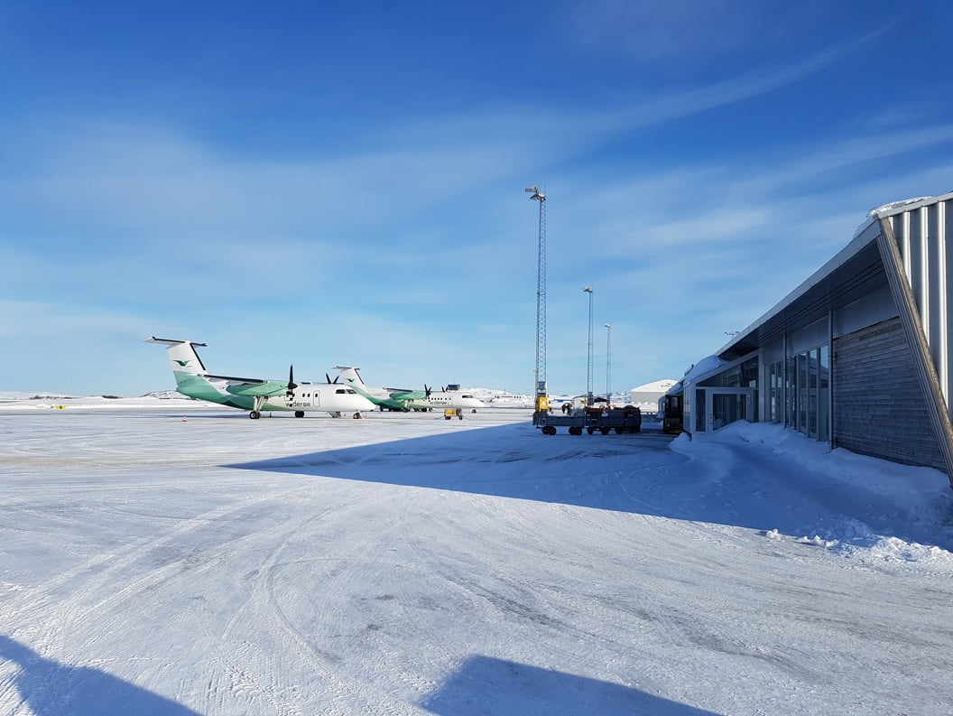 To fly på en snødekt rullebane ved kirkenes flyplass i Norge under klar blå himmel. Bygninger i nærheten viser moderne arkitektur.