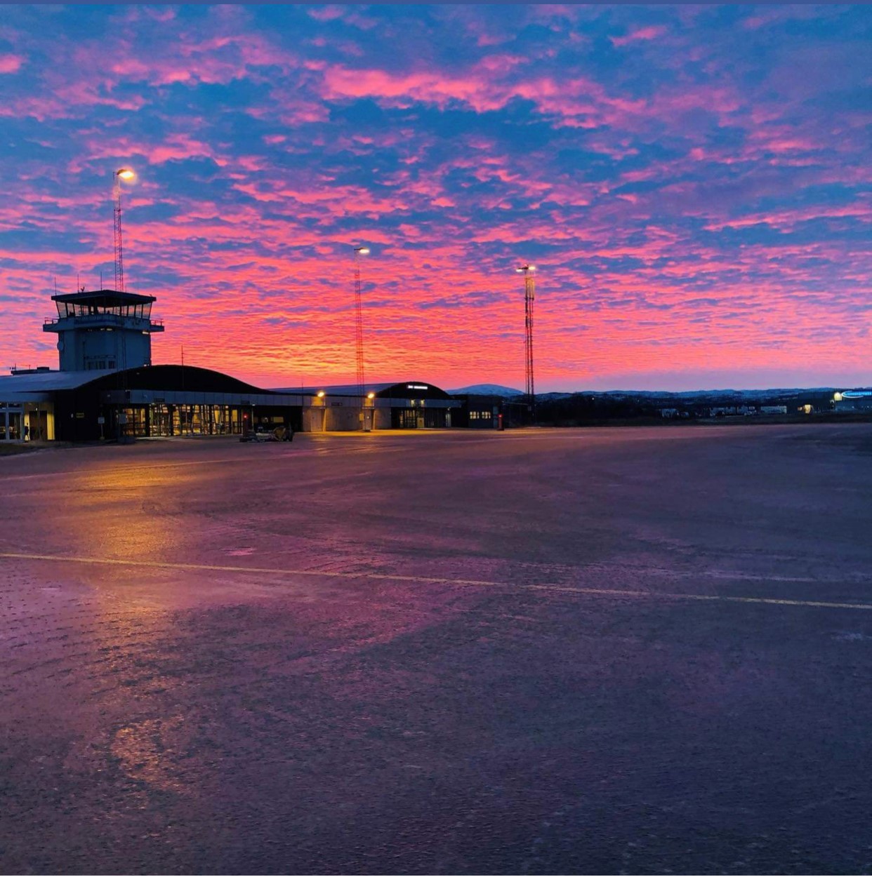 Lakselv flyplass ved solnedgang med fargerik himmel i rosa og blåtoner, terminalbygning og kontrolltårn.