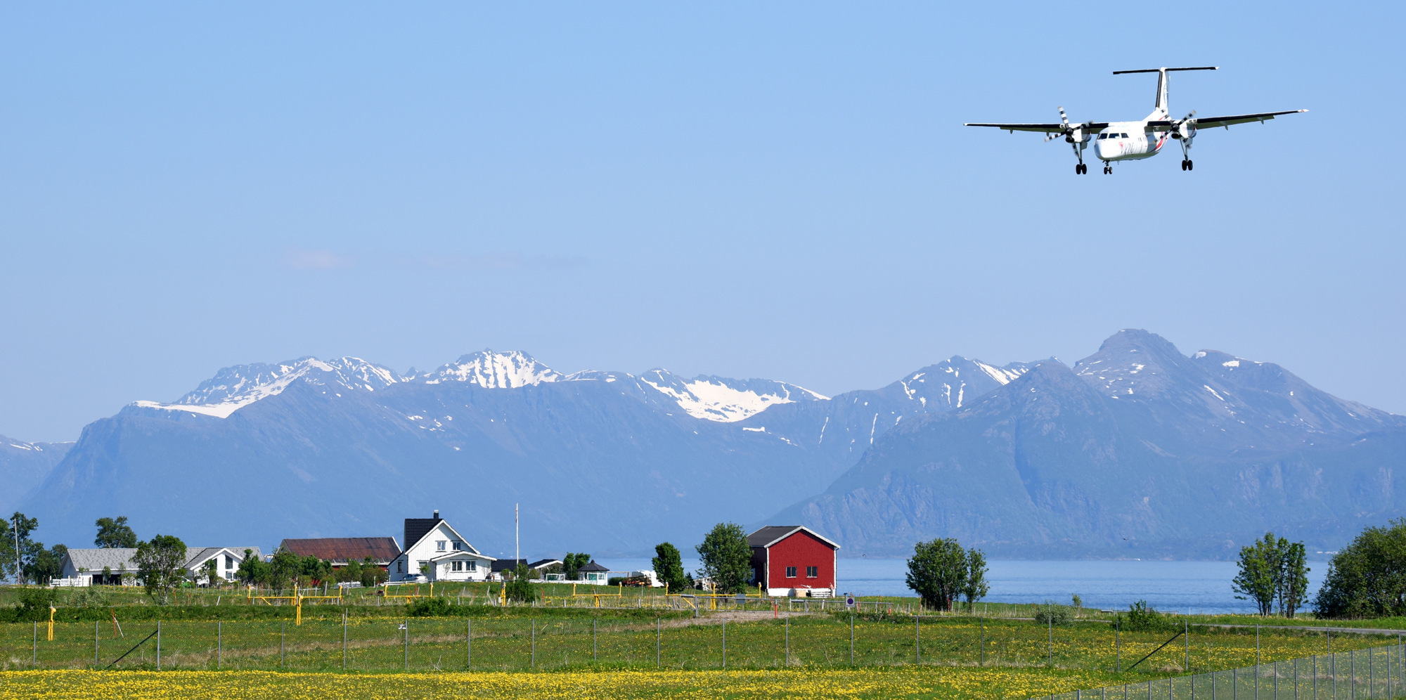 Fly som nærmer seg landingsstripen med fjellandskap i bakgrunnen og norske gårdshus i forgrunnen.