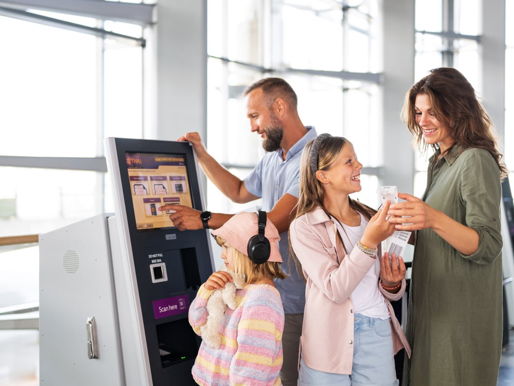 Family at the check-in kiosk at the airport, with mother, father, and two children checking in tickets at a digital terminal. Atmosphere of travel excitement and modern technology.