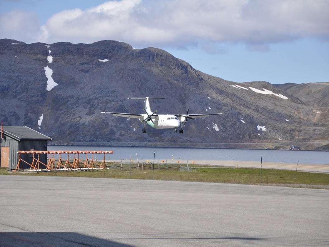 Fly som lander på Honningsvåg flyplass omgitt av fjellandskap i Norge, med klar blå himmel i bakgrunnen.