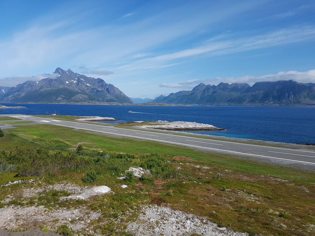 Runway at Svolvær Airport by the fjord with majestic mountains in the background under a blue sky in Northern Norway.