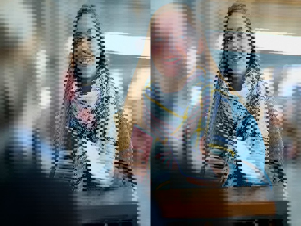 En dame med langt halvmørkt står foran en skranke på flyplassterminalen med passet sitt i hånden.