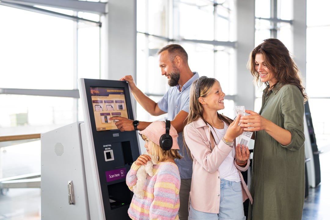 En familie med mann, dame og to barn, en litt større jente og en litt mindre jente står ved innsjekkingsautomaten i terminalen på Oslo lufthavn og sjekker inn.
