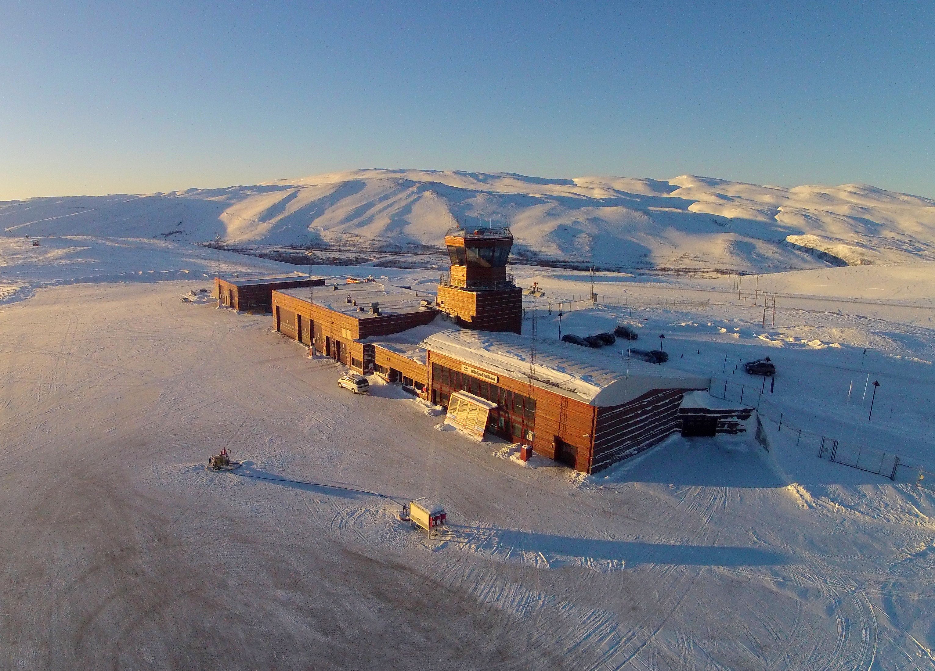 Båtsfjord lufthavn terminalbygning på en overskyet dag, med rullebane og gresskledde åser i bakgrunnen.