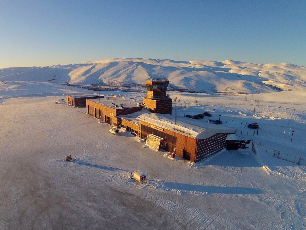 Båtsfjord lufthavn terminalbygning på en overskyet dag, med rullebane og gresskledde åser i bakgrunnen.