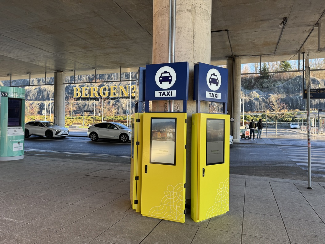 Bergen Airport taxi stand with digital kiosks and parked taxis, under a covered walkway