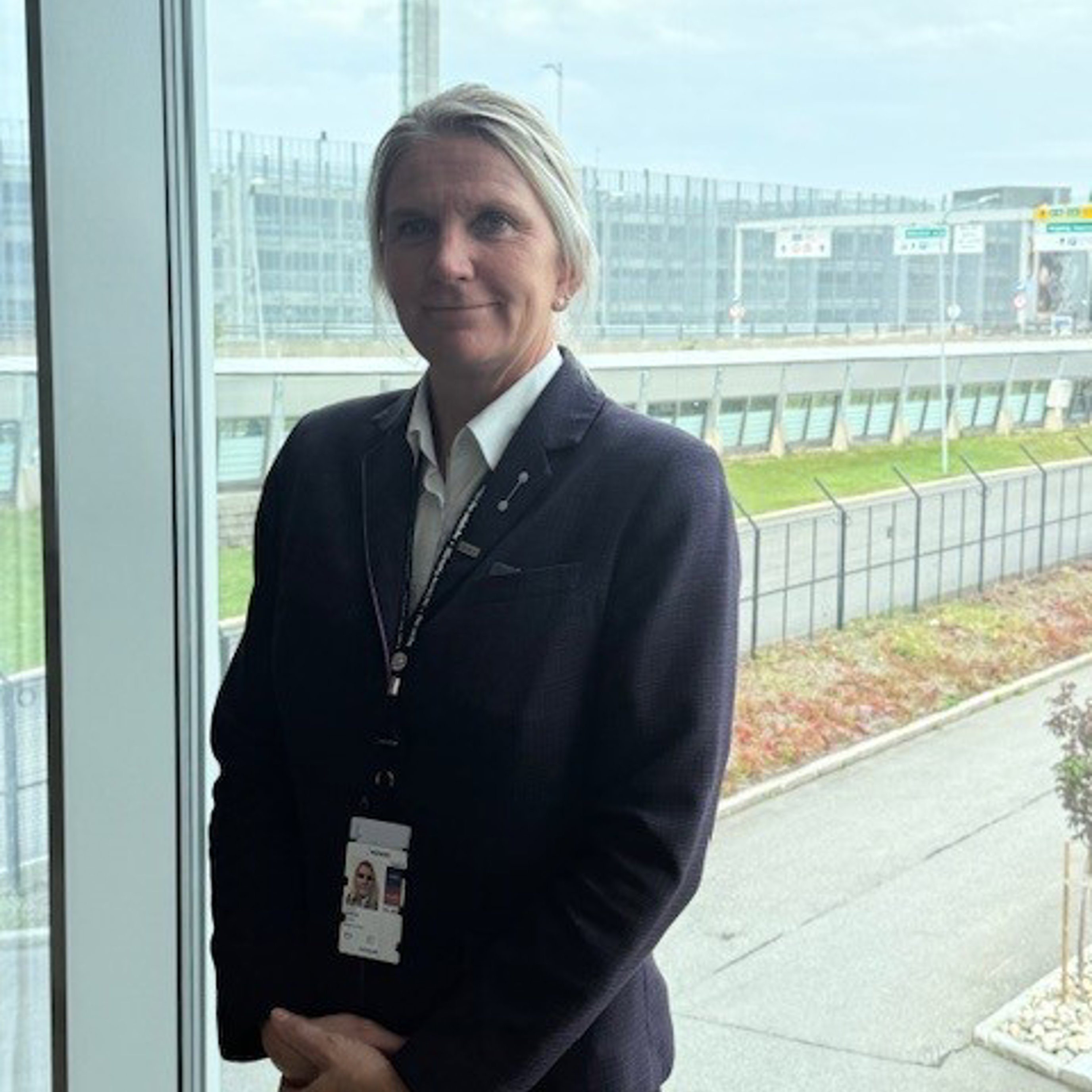 A person in a suit stands by a large window overlooking an airport, including an air traffic control tower in the background.