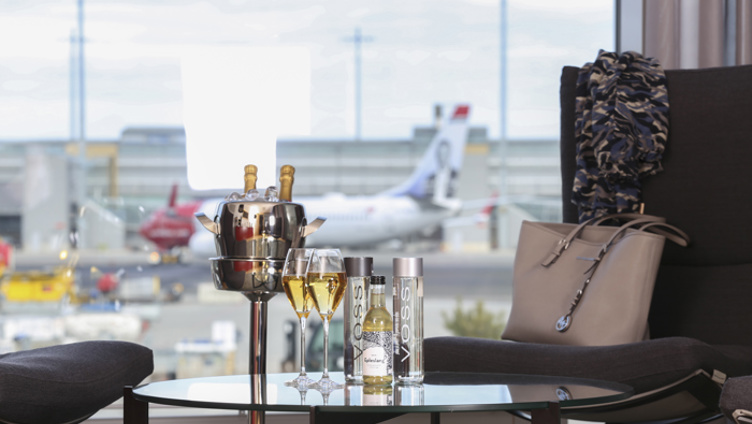 Luxurious airport lounge with a view of the runway, champagne, and Voss bottles on the table.