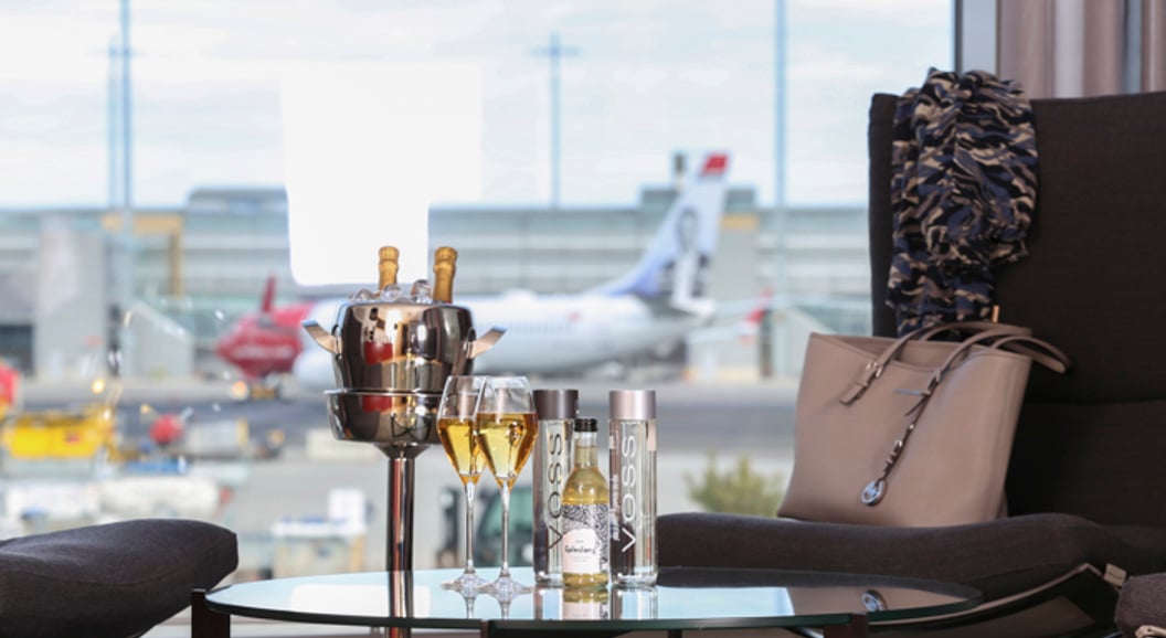 Luxurious airport lounge with a view of the runway, champagne, and Voss bottles on the table.