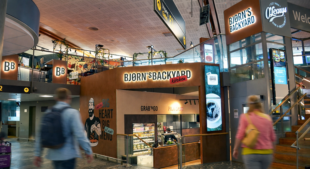 Bjorn's Backyard Kitchen restaurant entrance in a shopping mall, featuring a mural of a bearded man holding food, with slogans "Big Heart Big Menu" and "Grab 'N Go, Pick Up