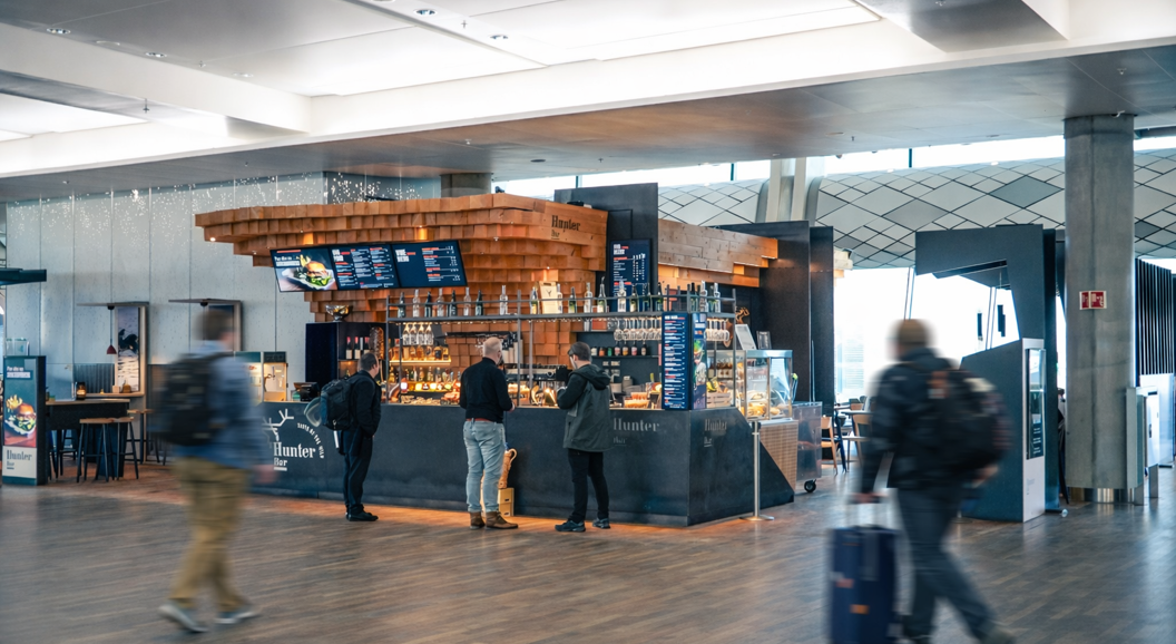 Modern bar interior with wood accents and sleek design at Hunter Bar, showcasing a digital menu, hanging glasses, and a display case with food items