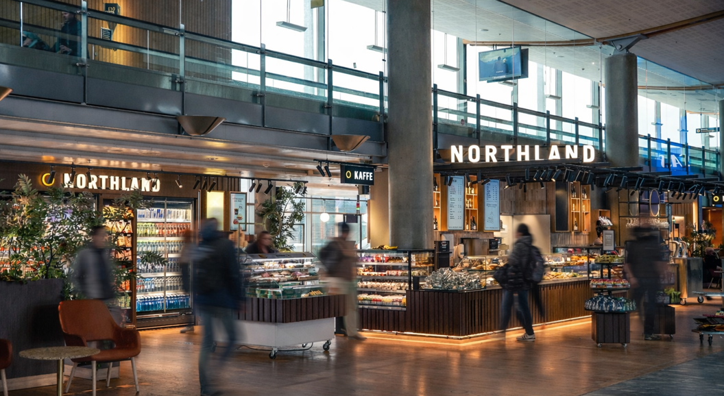People browsing food selections at a modern airport deli counter with various packaged goods and fresh items