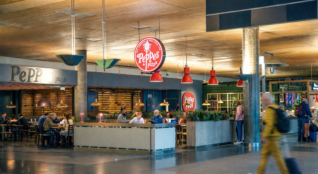 Person slicing a pizza topped with arugula and prosciutto on a white plate