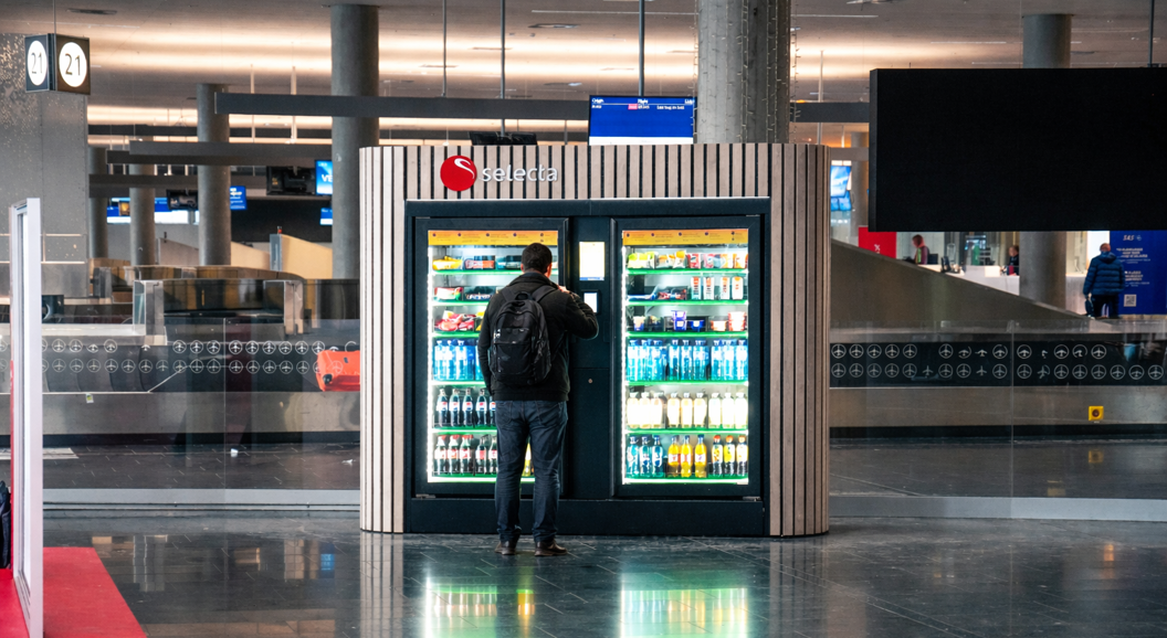 Vending machine filled with assorted snacks and candy bars, including popular brands, with illuminated selection panel