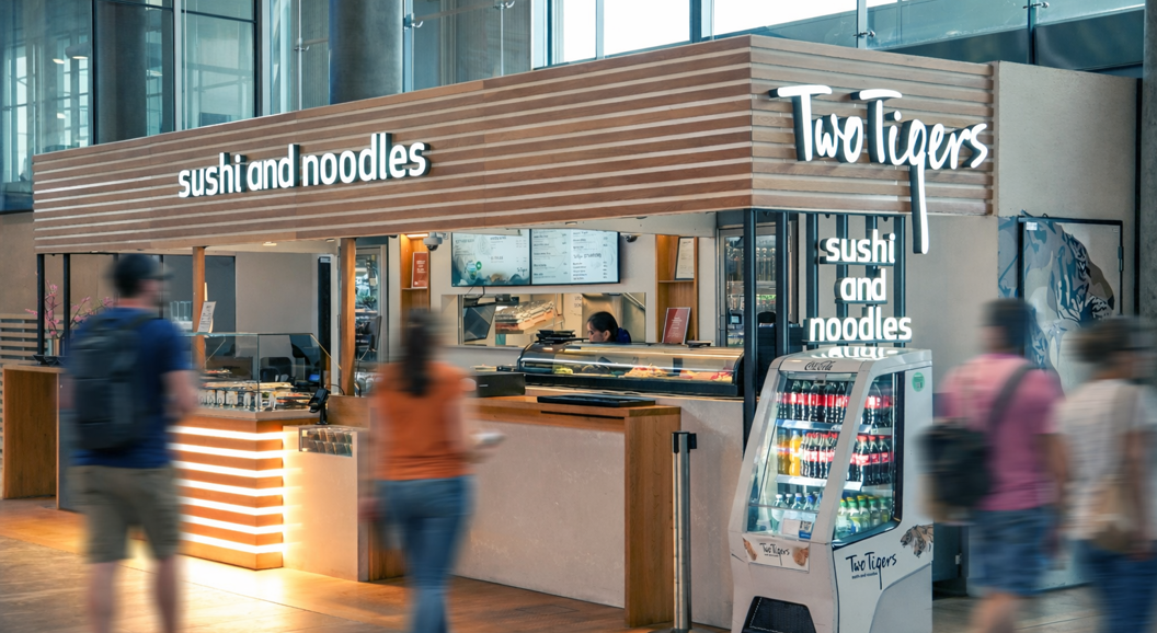 Assorted sushi platters in to-go containers with fresh nigiri and rolls, displayed on a wooden counter at a sushi restaurant