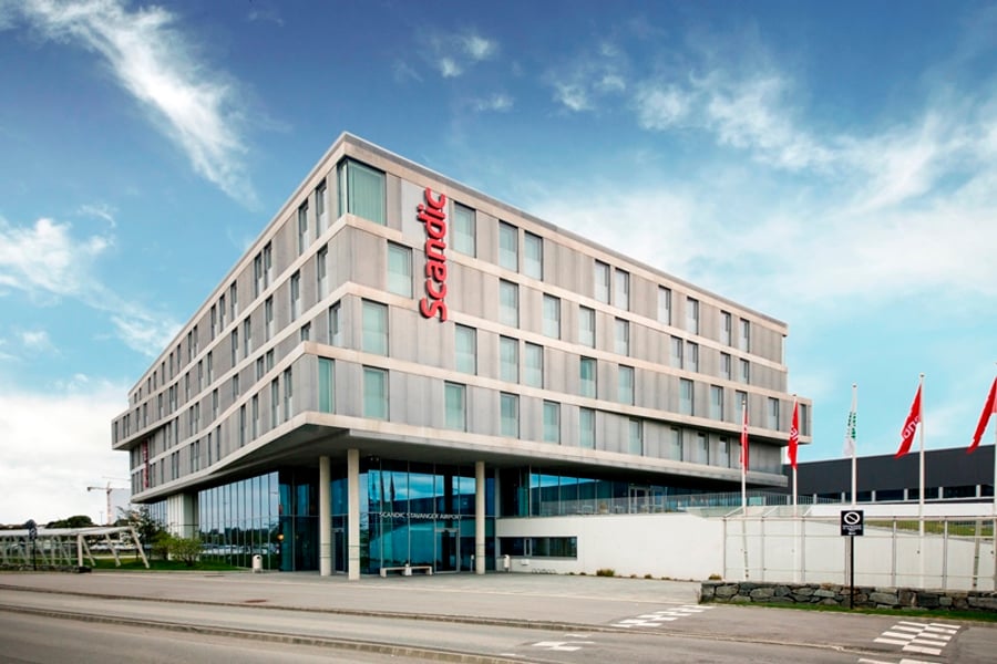 Moderne Scandic-hotellfasade nær Stavanger Lufthavn, omgitt av blå himmel og flagg.
