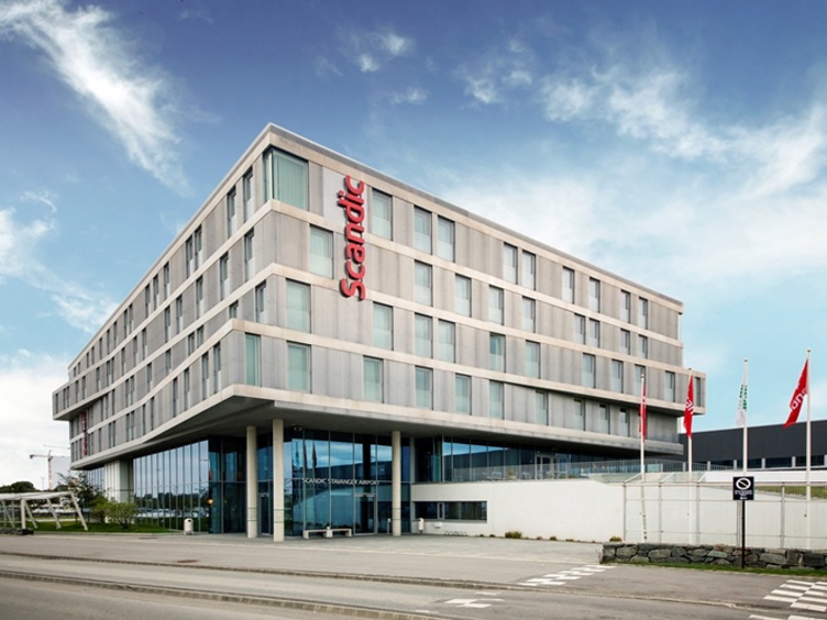 Moderne Scandic-hotellfasade nær Stavanger Lufthavn, omgitt av blå himmel og flagg.