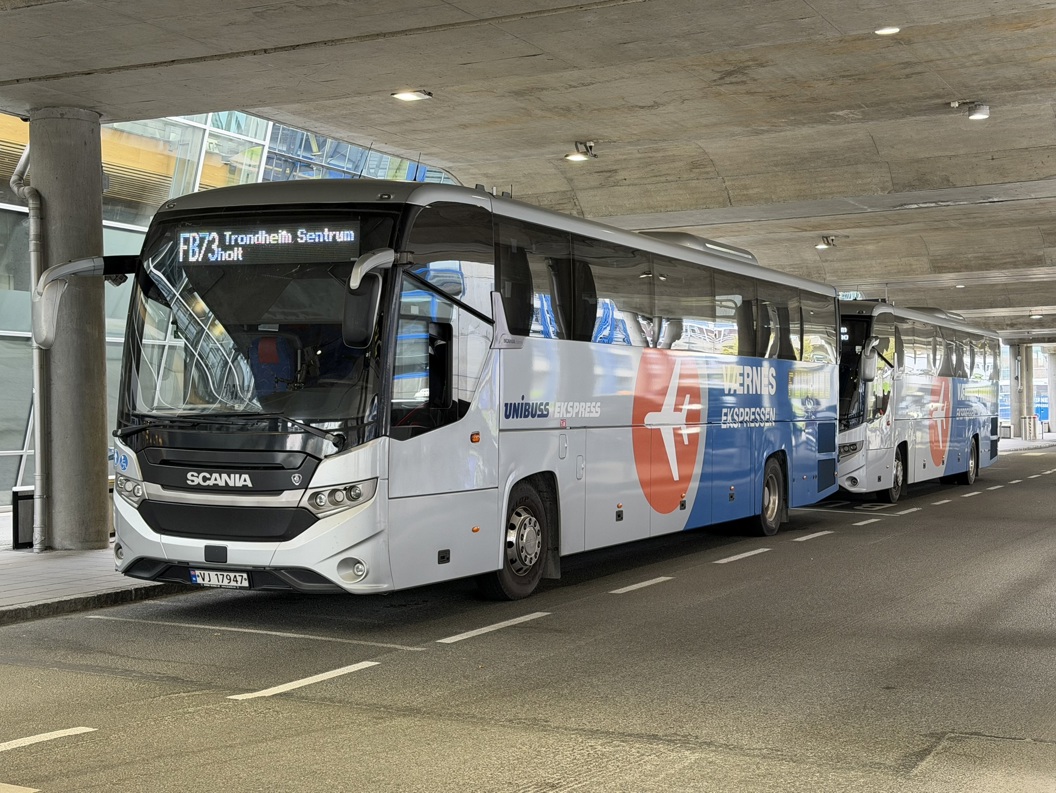 Two modern Scania buses parked at a terminal under a concrete overhang, featuring "Værnes Ekspressen" branding, with destination signage for Trondheim Sentrum, route FB73